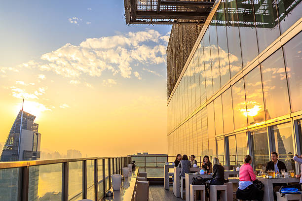 Hong Kong, China - January 1, 2016: people drink and enjoy the skyline of Victoria Harbor at sunset from the rooftop of Eye Bar, inside iSquare shopping center on Nathan Road in Tsim Sha Tsui, Kowloon
